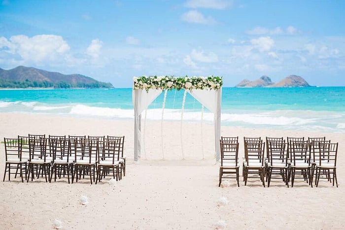 Hawaii beach wedding setup with 30 chairs and an arch with flowers